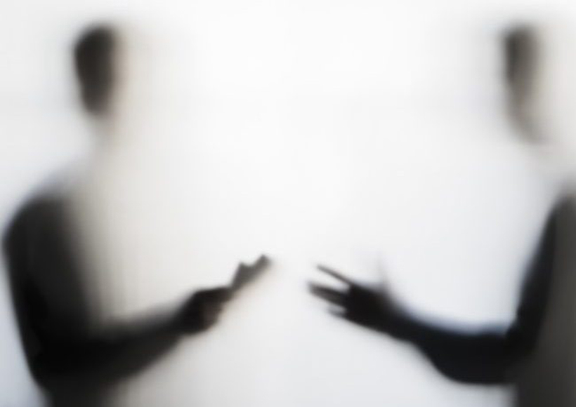 two blurred figures of humans talking in the shadows